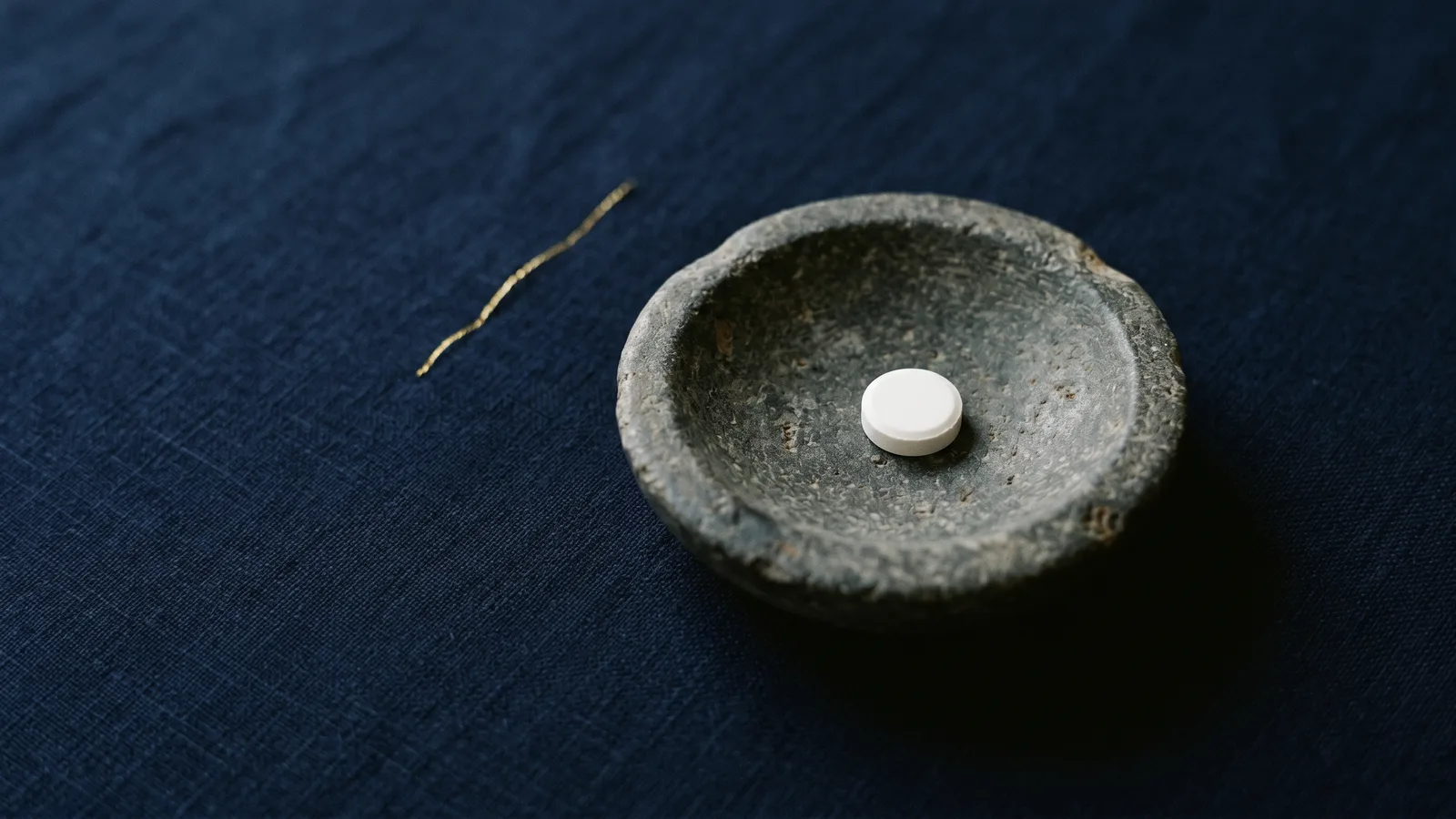 A single white pill in a shallow stone dish