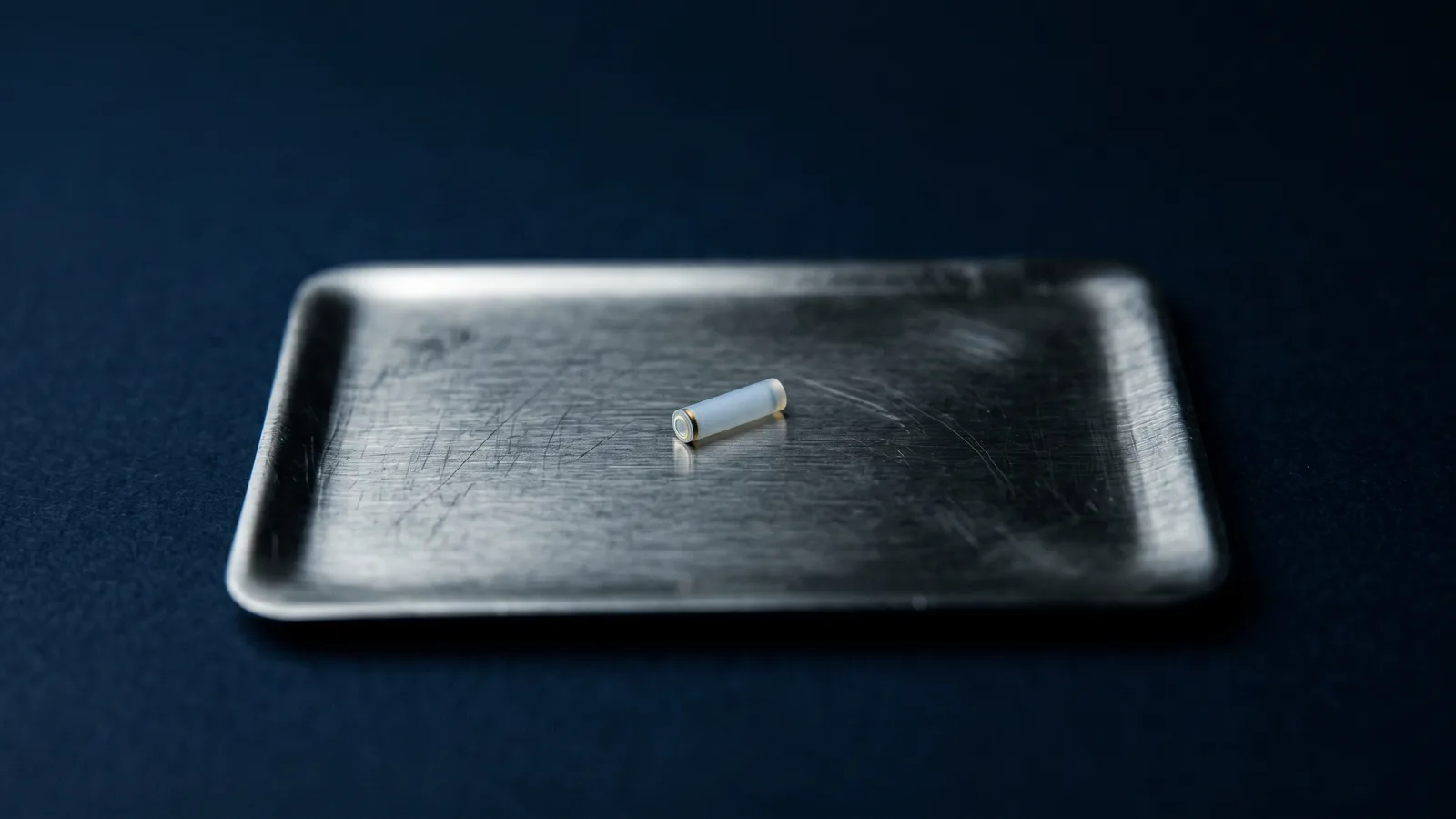 A tiny cylindrical polymer implant on a steel tray