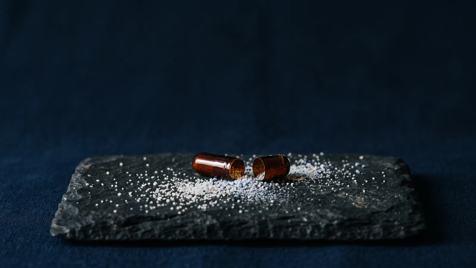 A half-open capsule with granules scattered across dark stone