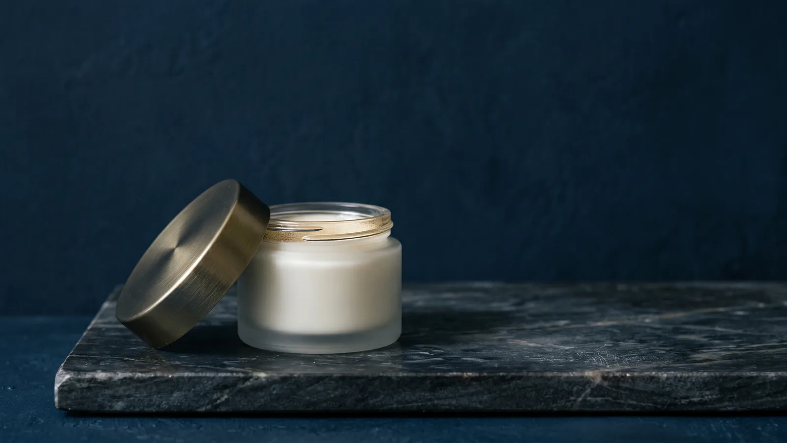 An unlabeled cosmetic jar with its lid ajar on dark marble