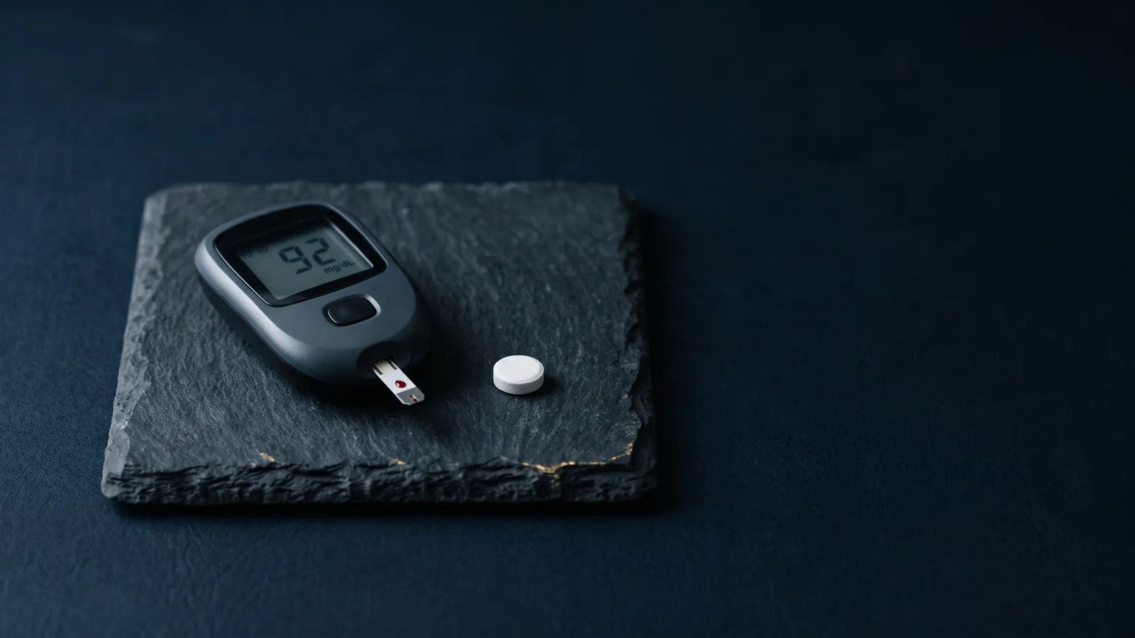 A glucose meter and tablet on dark slate