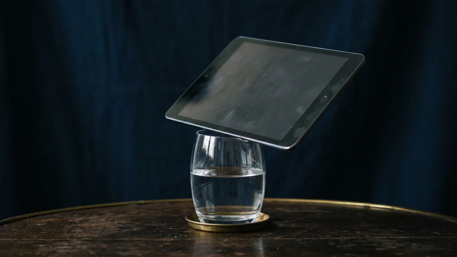 A tablet balanced on the rim of a glass of water