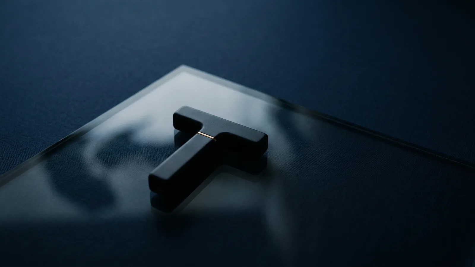A small T-shaped device silhouetted under glass