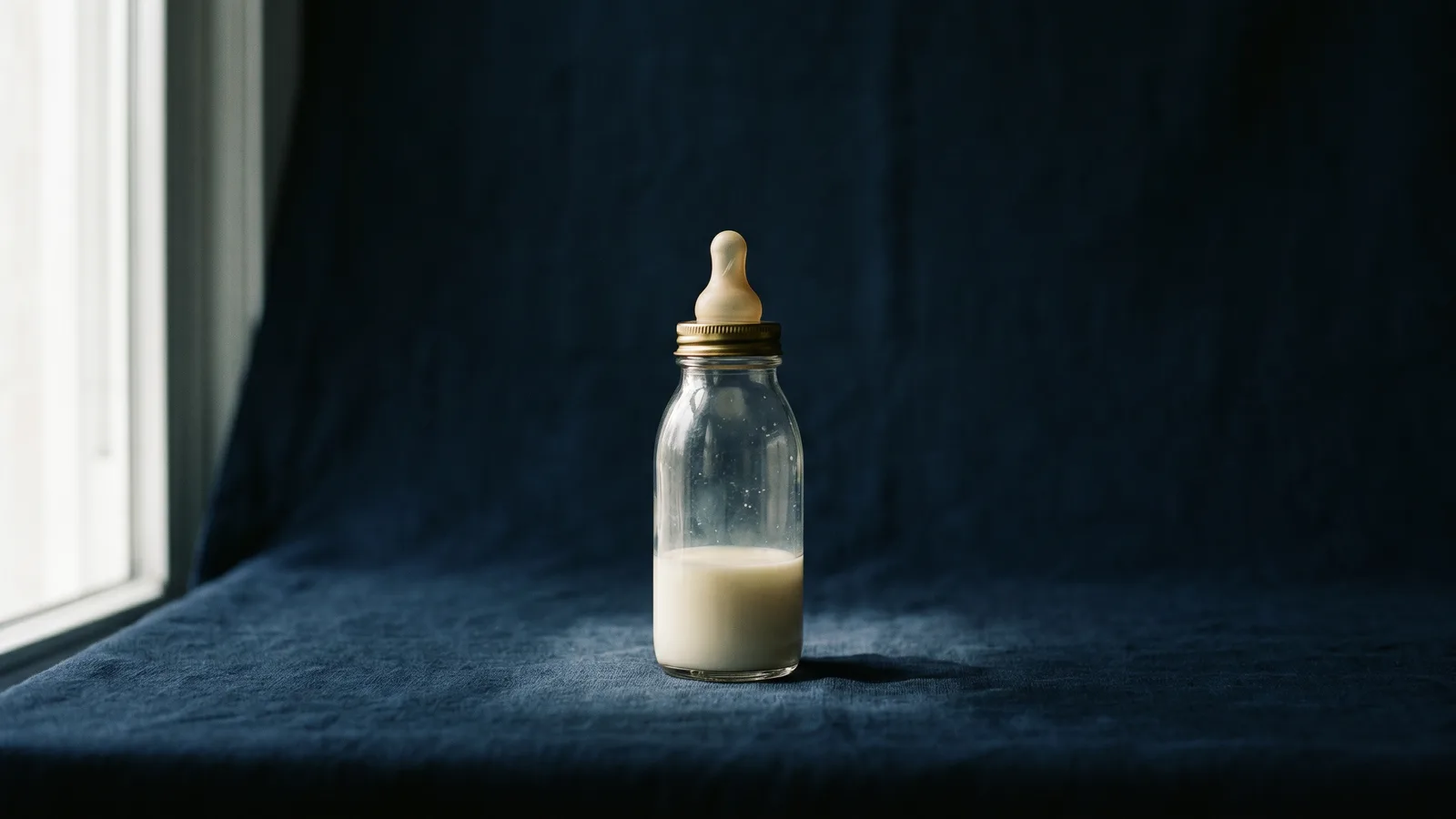 A single glass baby bottle in a shaft of soft light