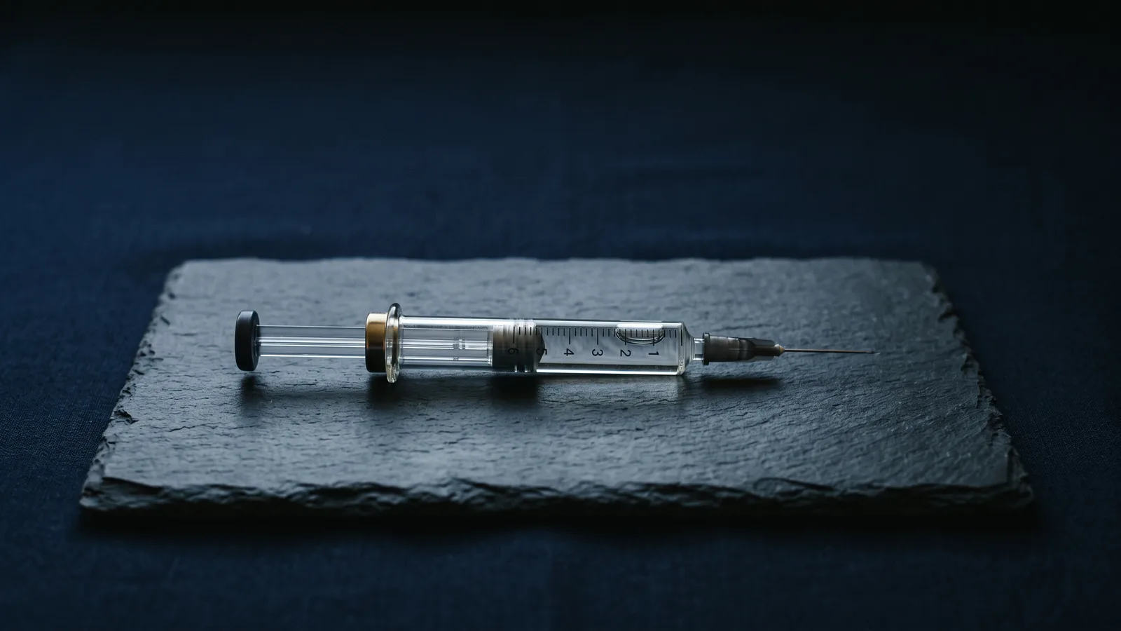 A glass injection pen resting on dark slate