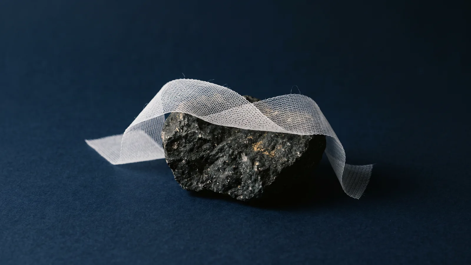 A fine white surgical mesh ribbon draped over dark stone