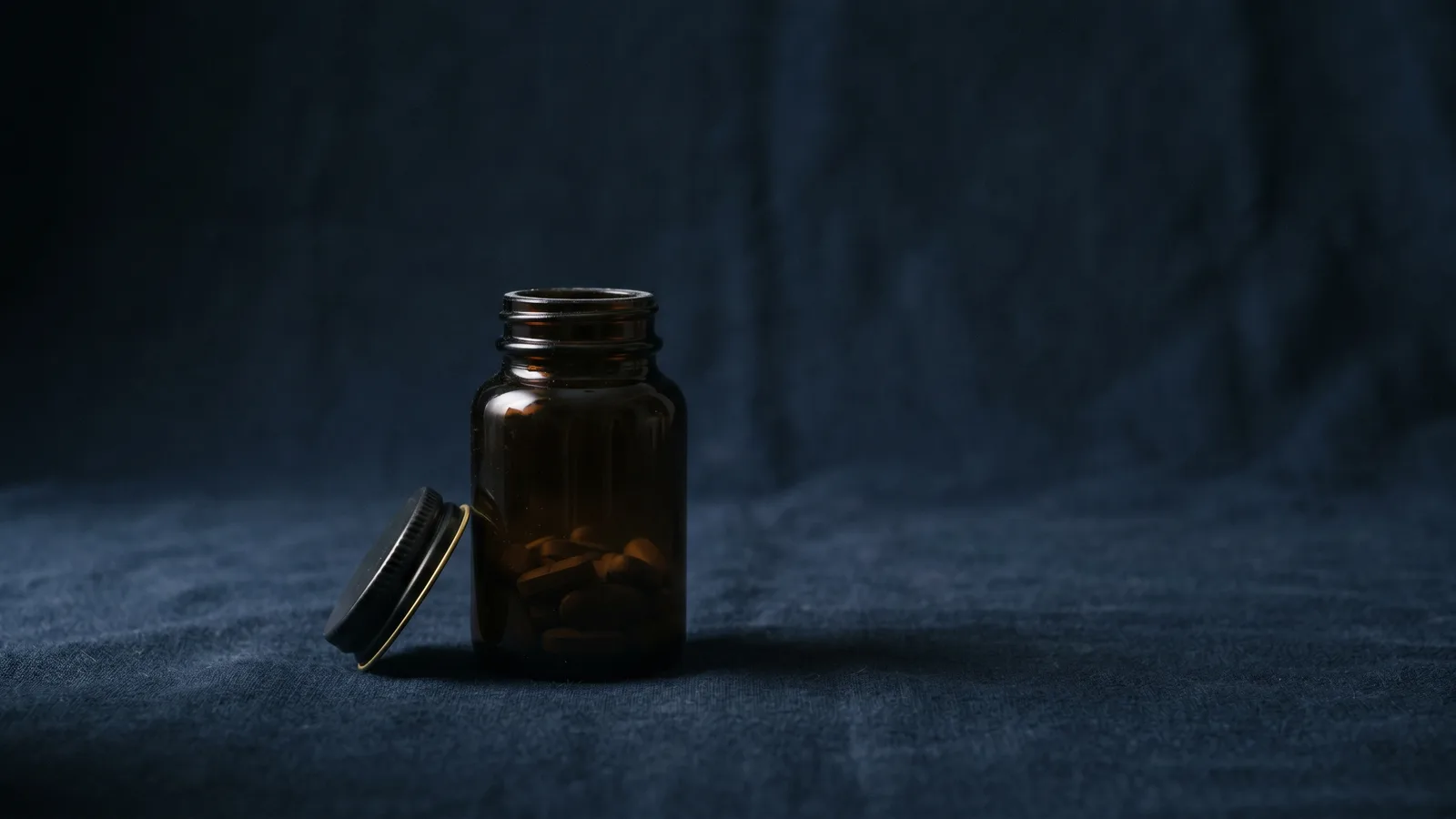A tablet bottle with its cap ajar in low-key light